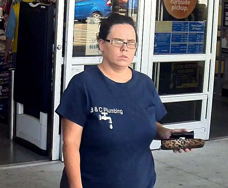 Photo of female theft suspect exiting New Caney Wal-Mart wearing black framed glasses and a B&C navy blue plumbing t-shirt.